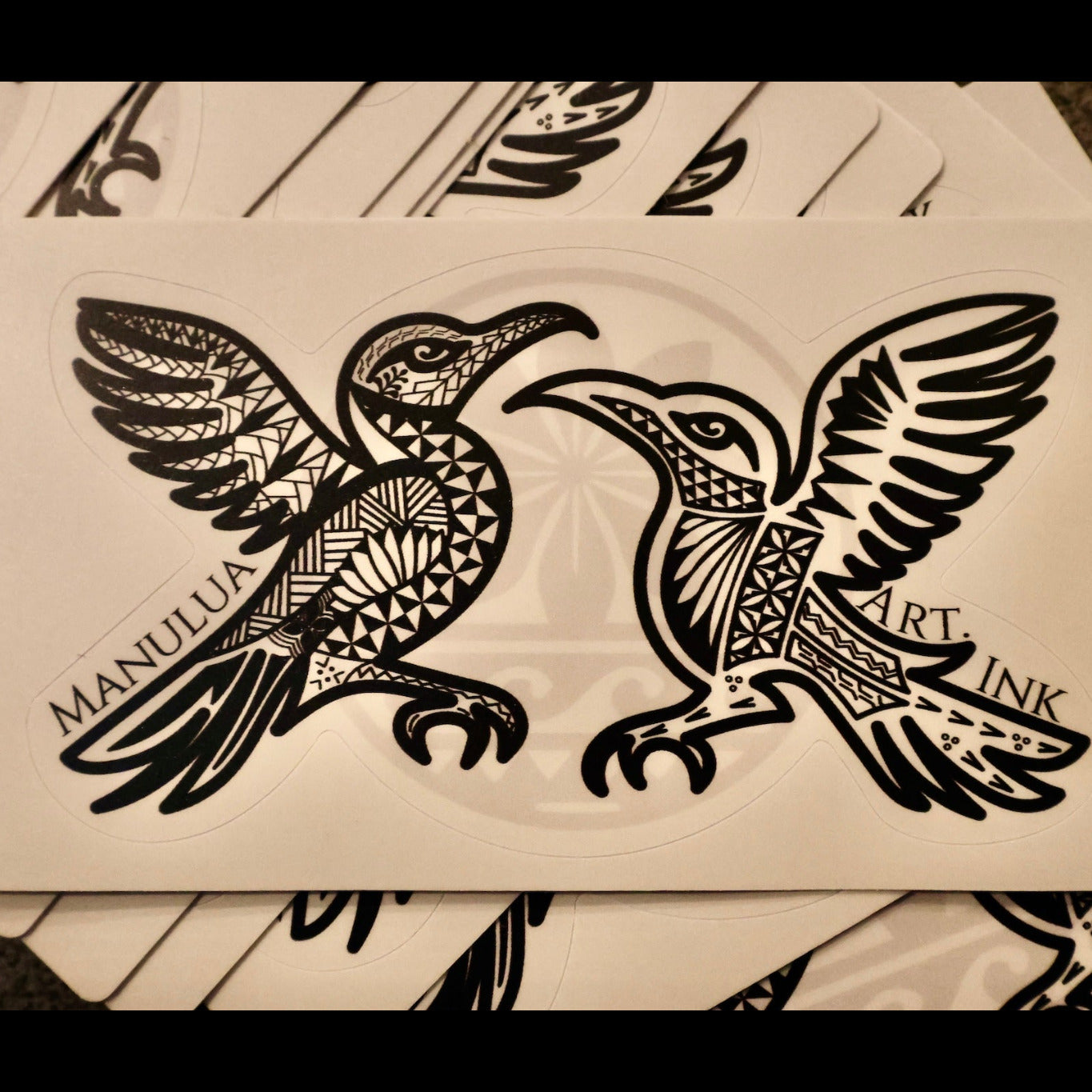 Two intricately designed birds on a sticker surface with 'Manulua Art Ink' branding.