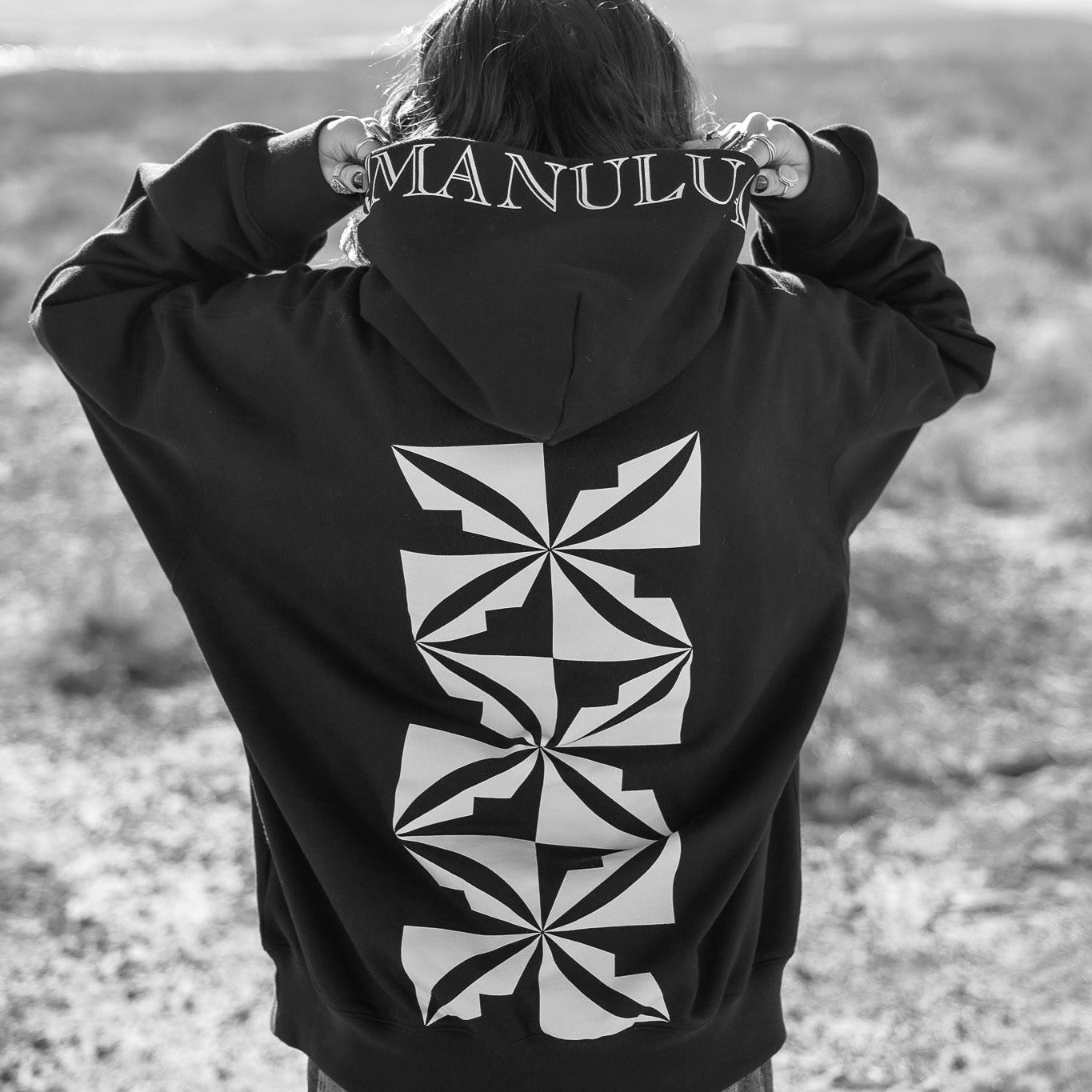 Person wearing a black hoodie with geometric design and text on the back, standing outdoors.