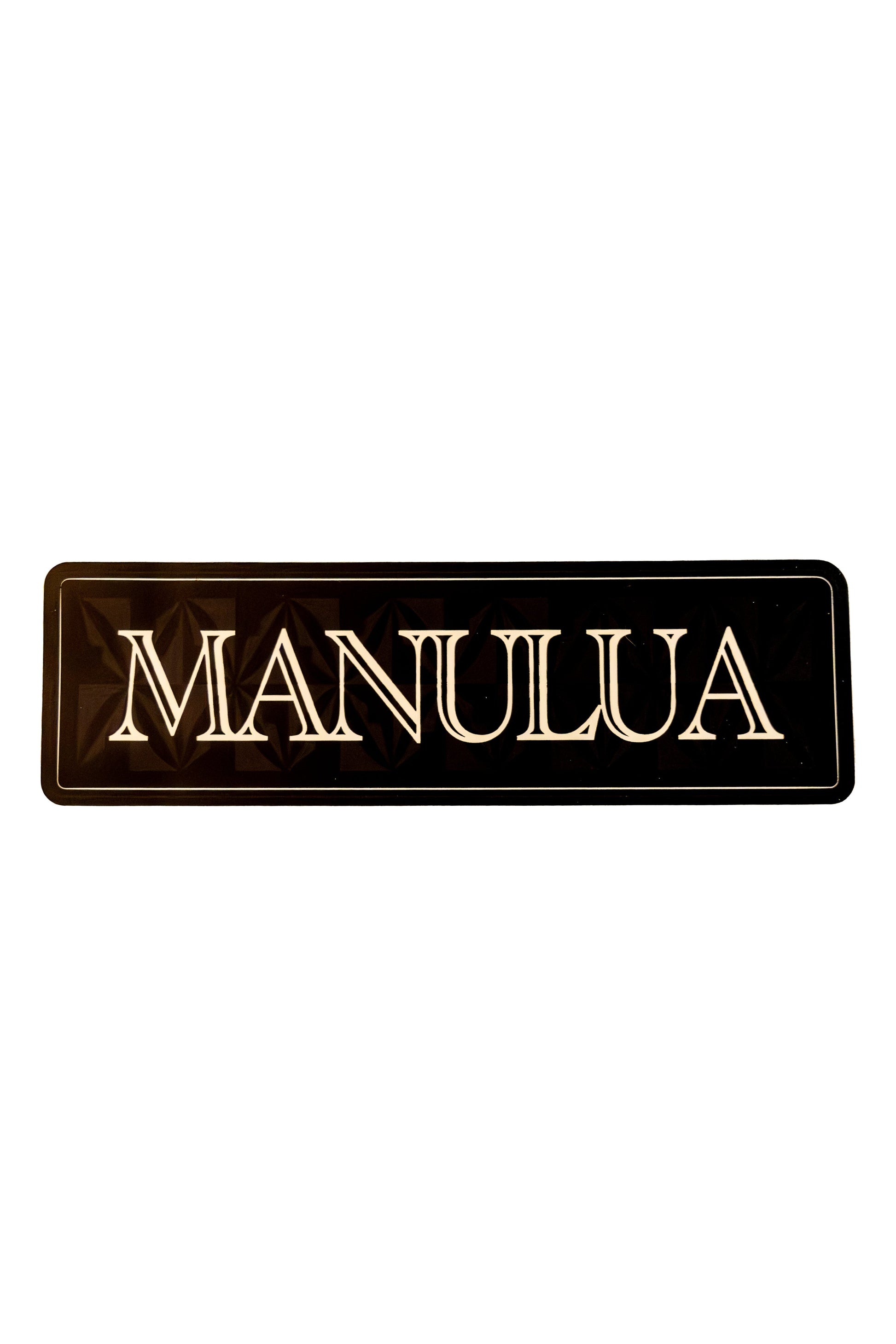 Black rectangular sign with 'MANULUA' in gold on a white background