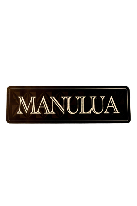 Black rectangular sign with 'MANULUA' in gold on a white background