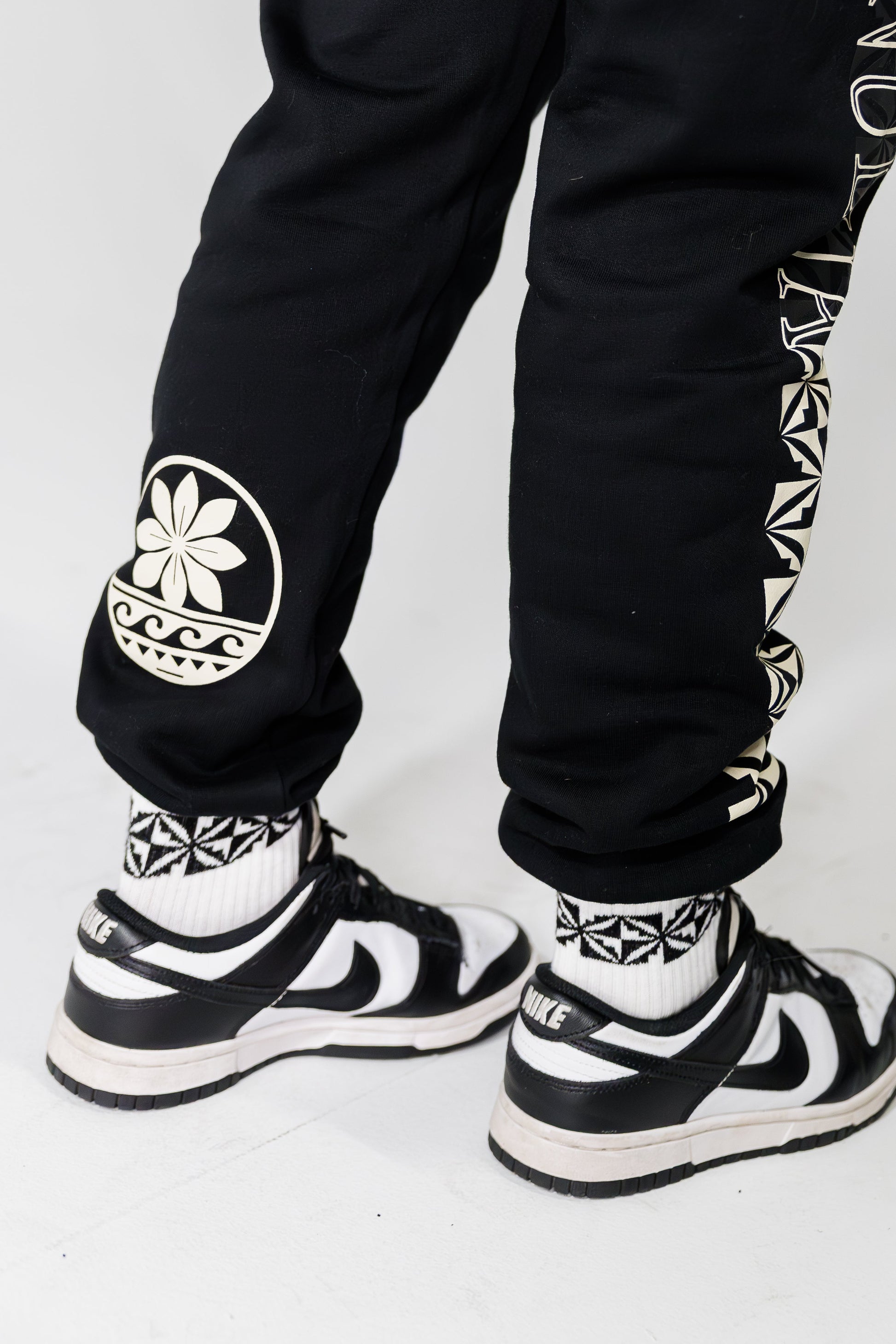 Black pants with white patterns and black and white sneakers on a white background