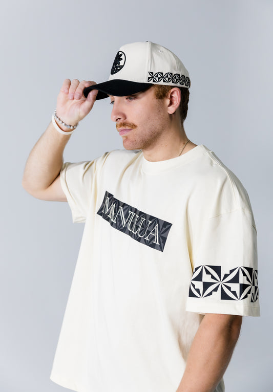Man wearing a white t-shirt with black graphics and text, holding a cap.