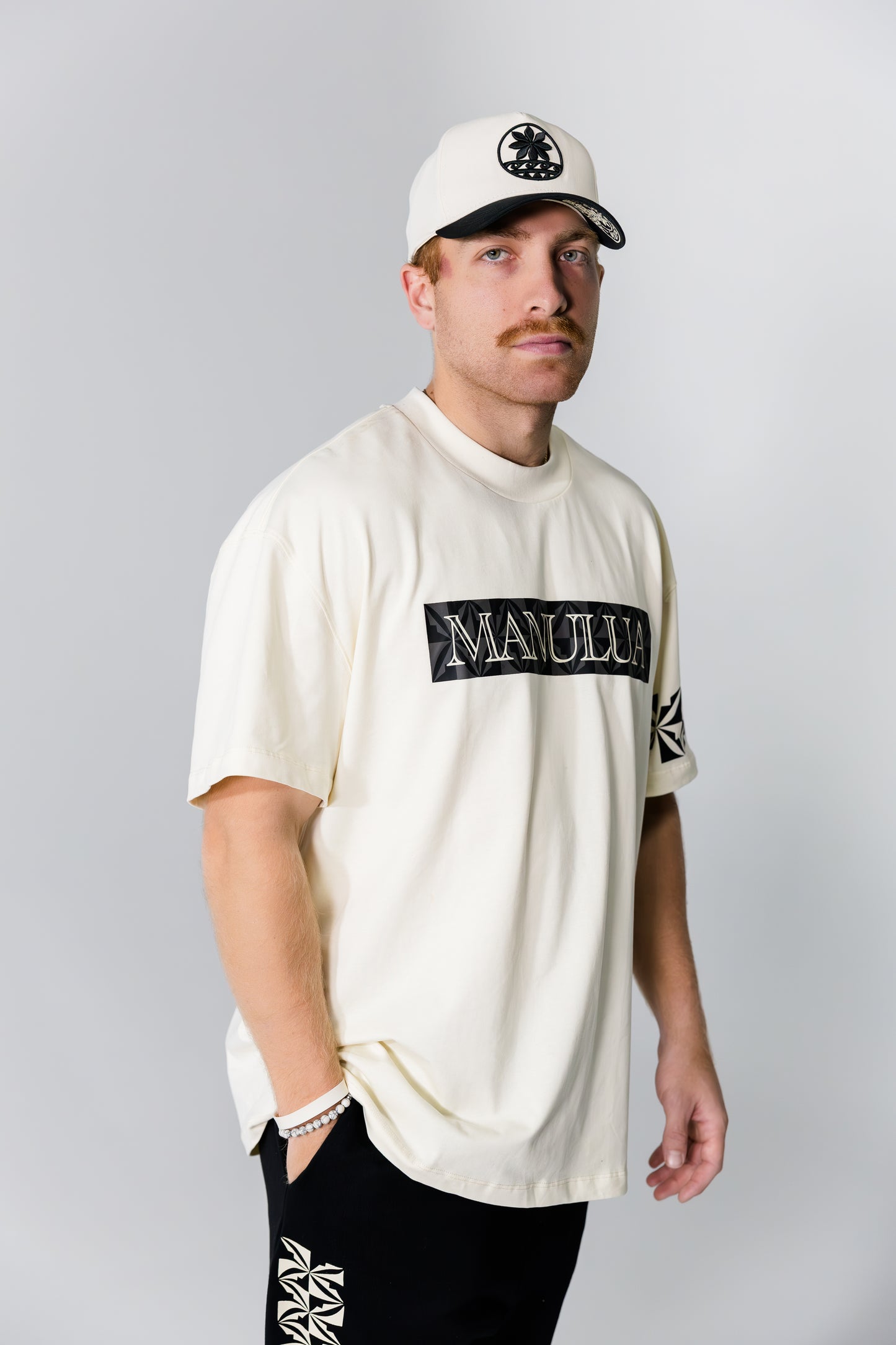 Man wearing a white t-shirt with branding and a cap on a gray background