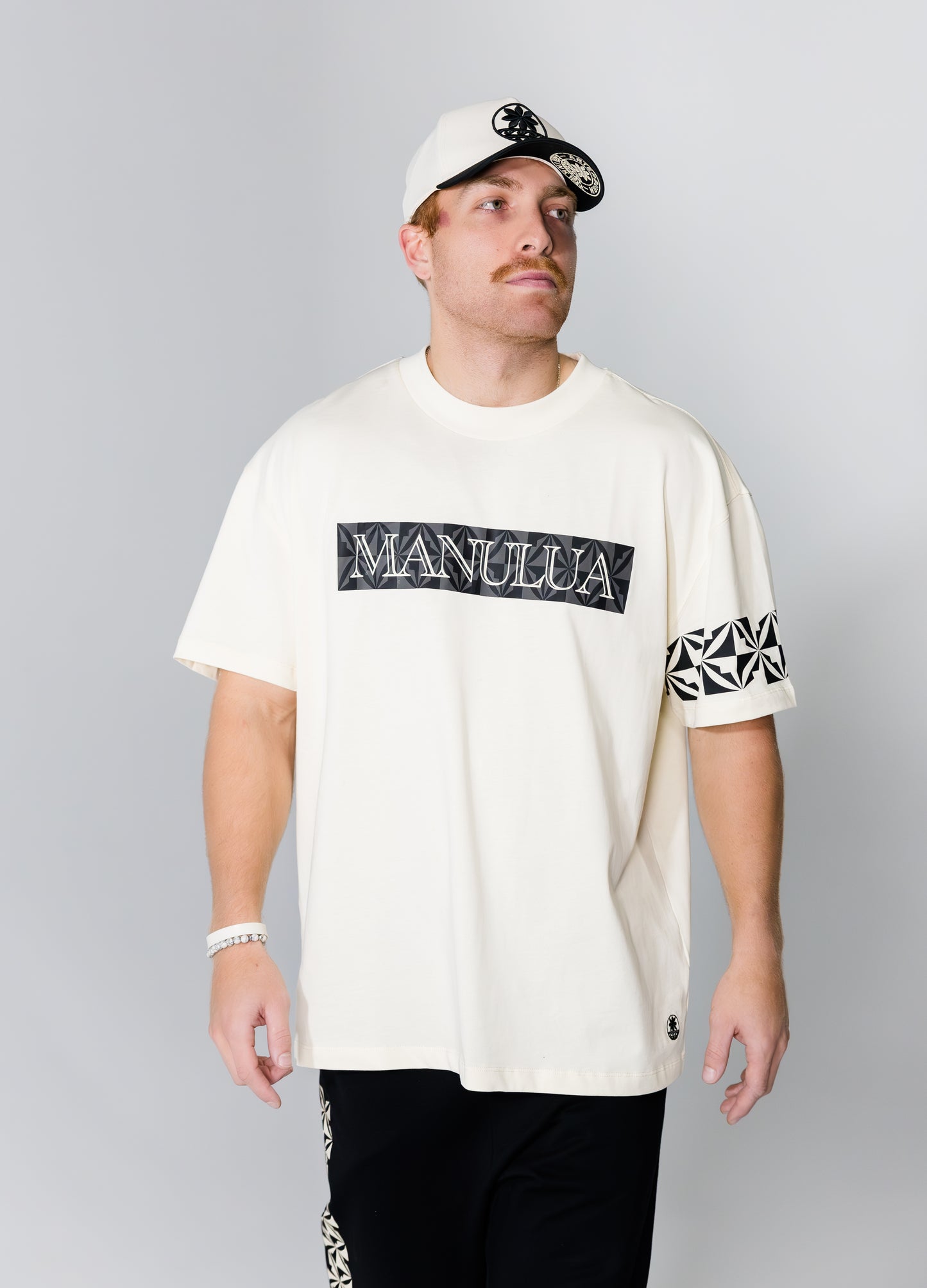 Man wearing a white t-shirt with 'Manulua' branding on a gray background