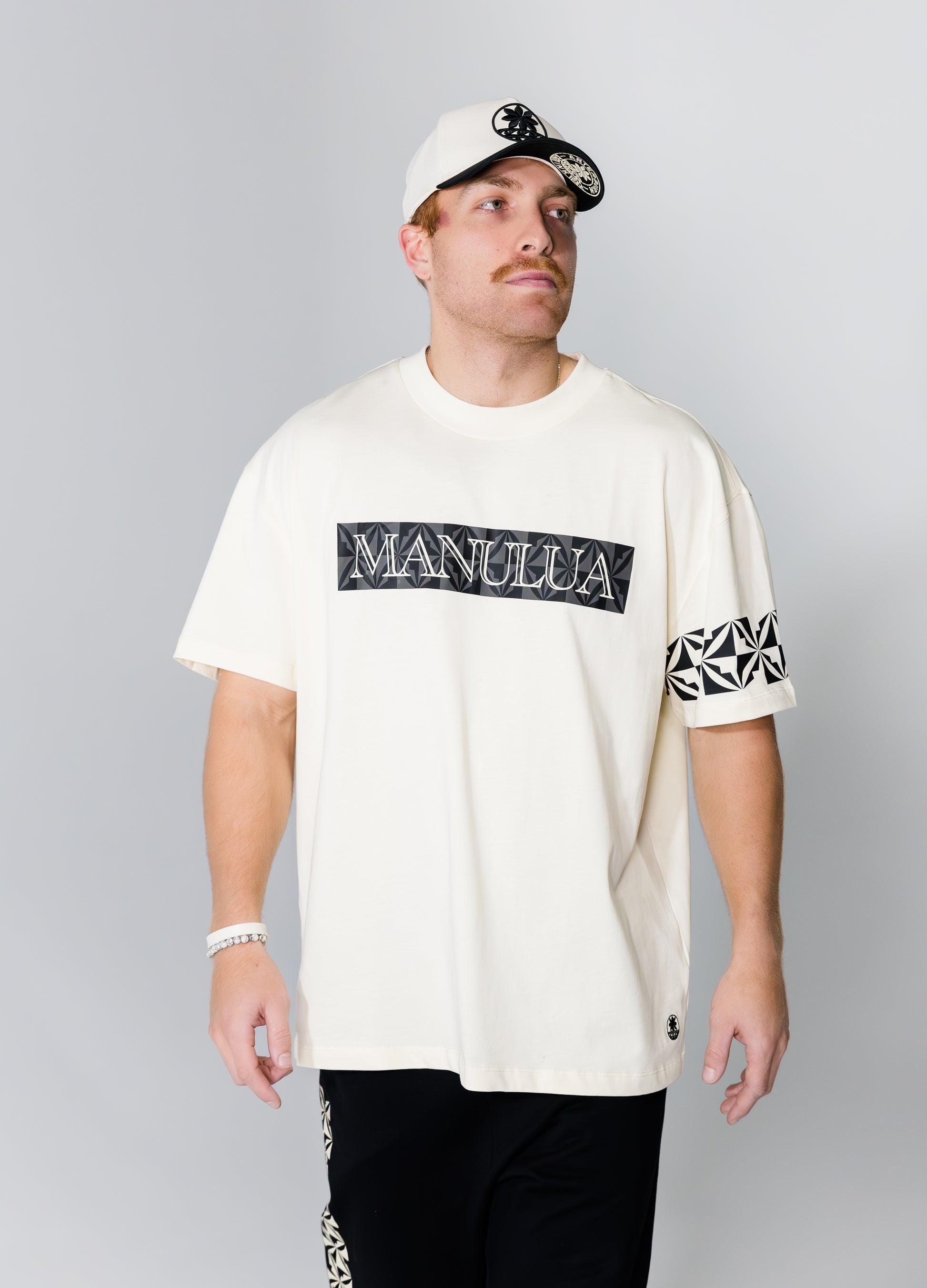 Man wearing a white t-shirt with 'Manulua' branding on a gray background