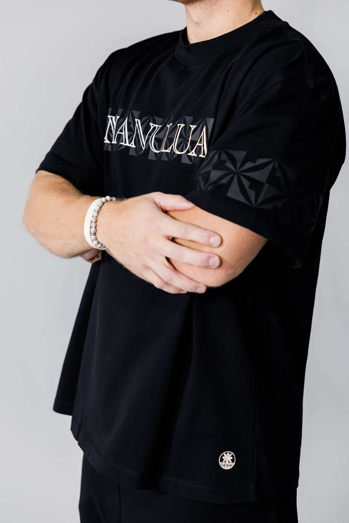 Person wearing a black t-shirt with 'Manulua' logo on a gray background