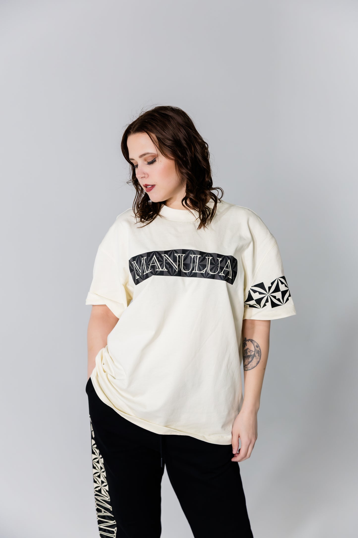 Person wearing a white oversized t-shirt with 'Manulua' branding on a gray background