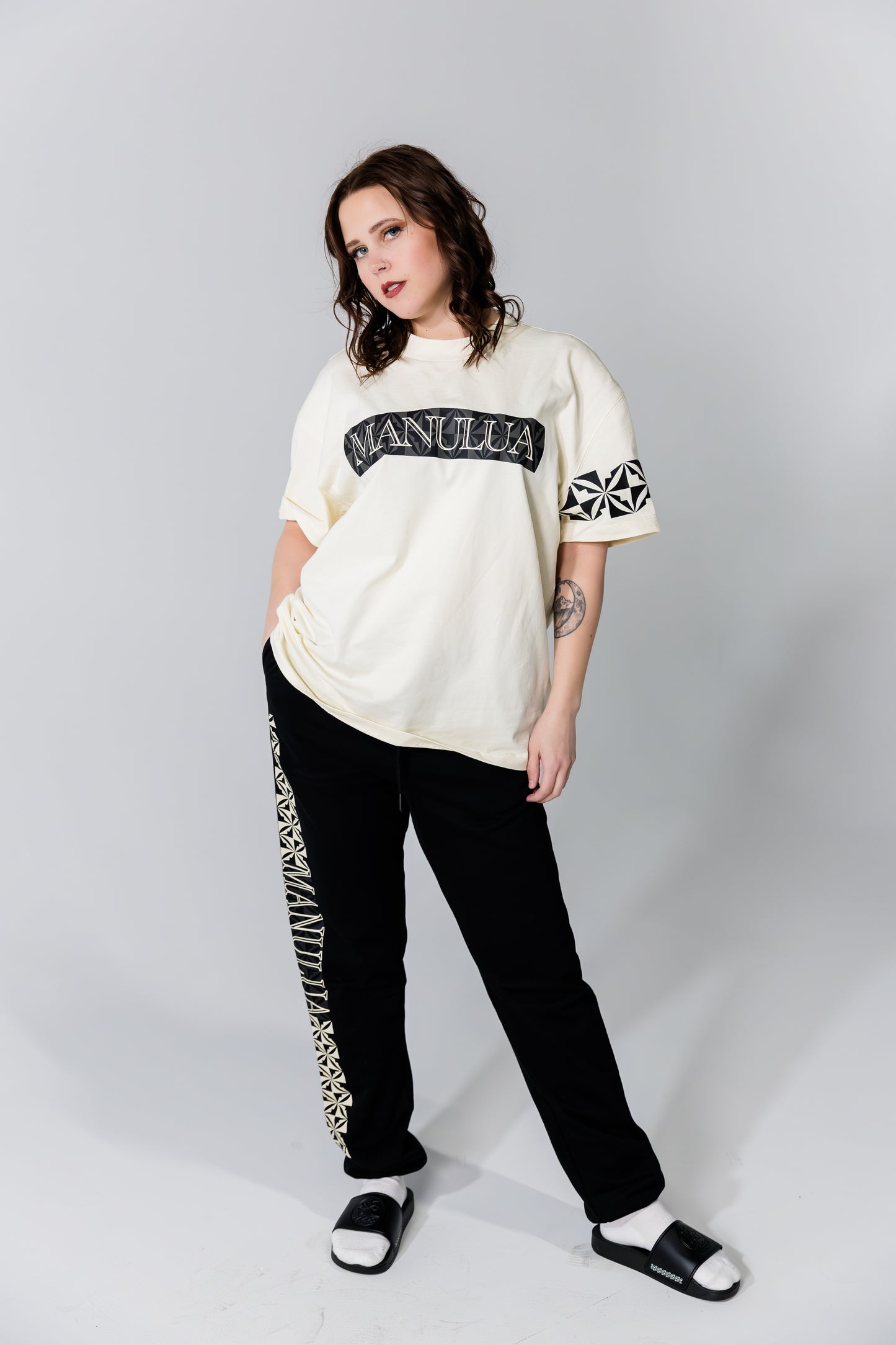 Person wearing a white oversized t-shirt with text and black pants with white text on a plain background