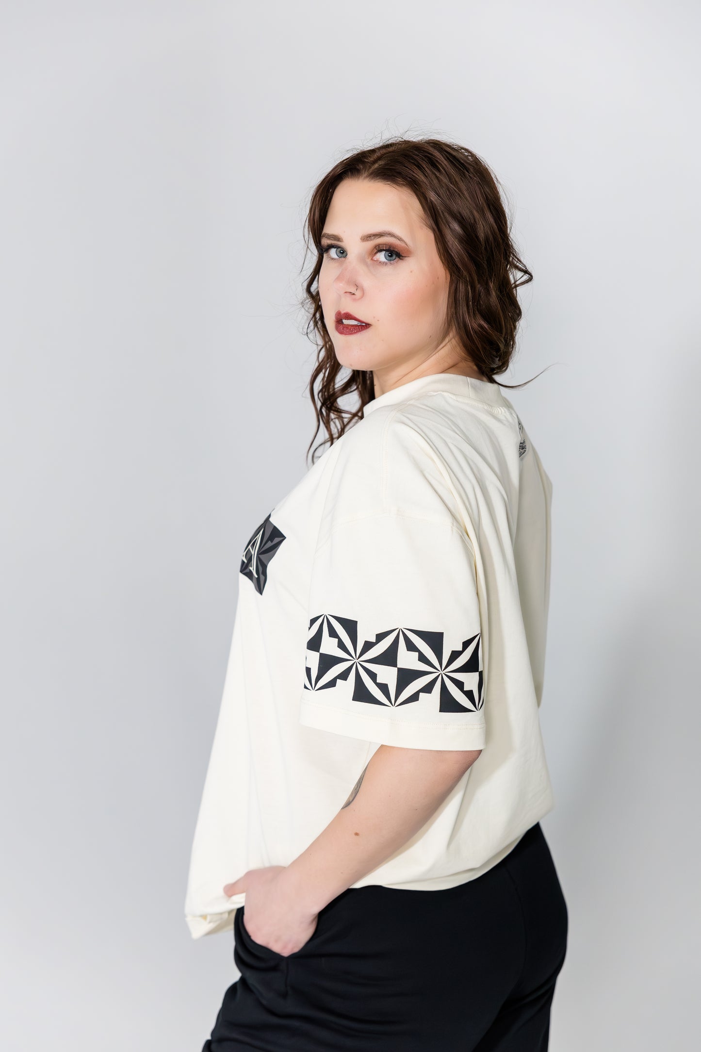 Woman wearing a white t-shirt with black geometric designs on a plain background