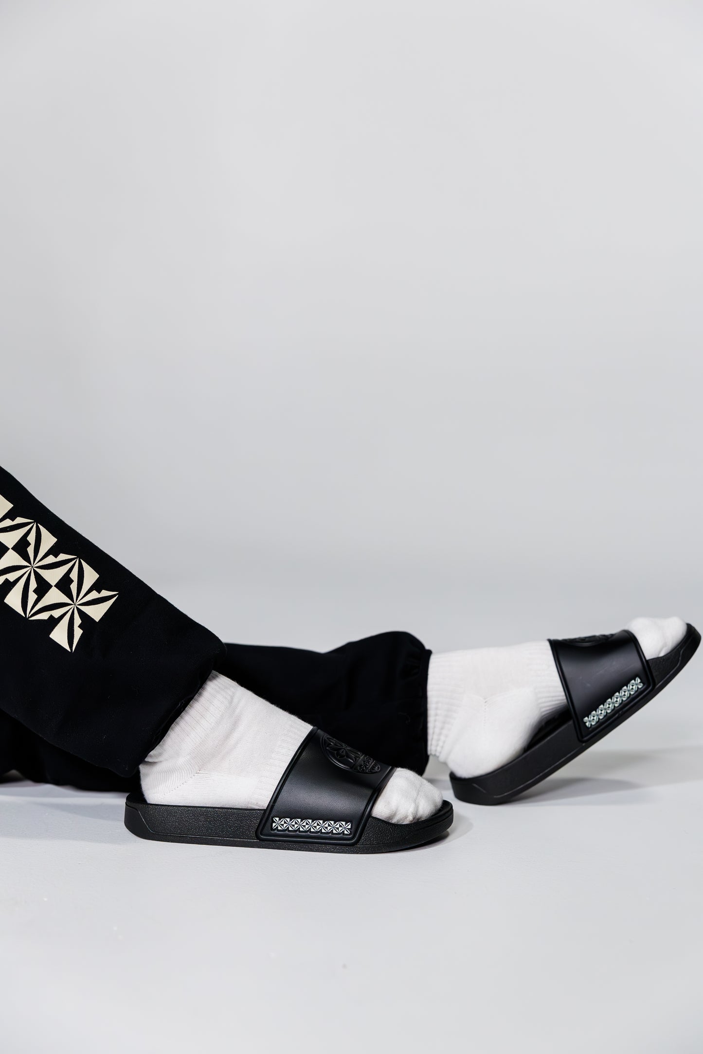 Black and white sandals worn with black pants on a light gray background