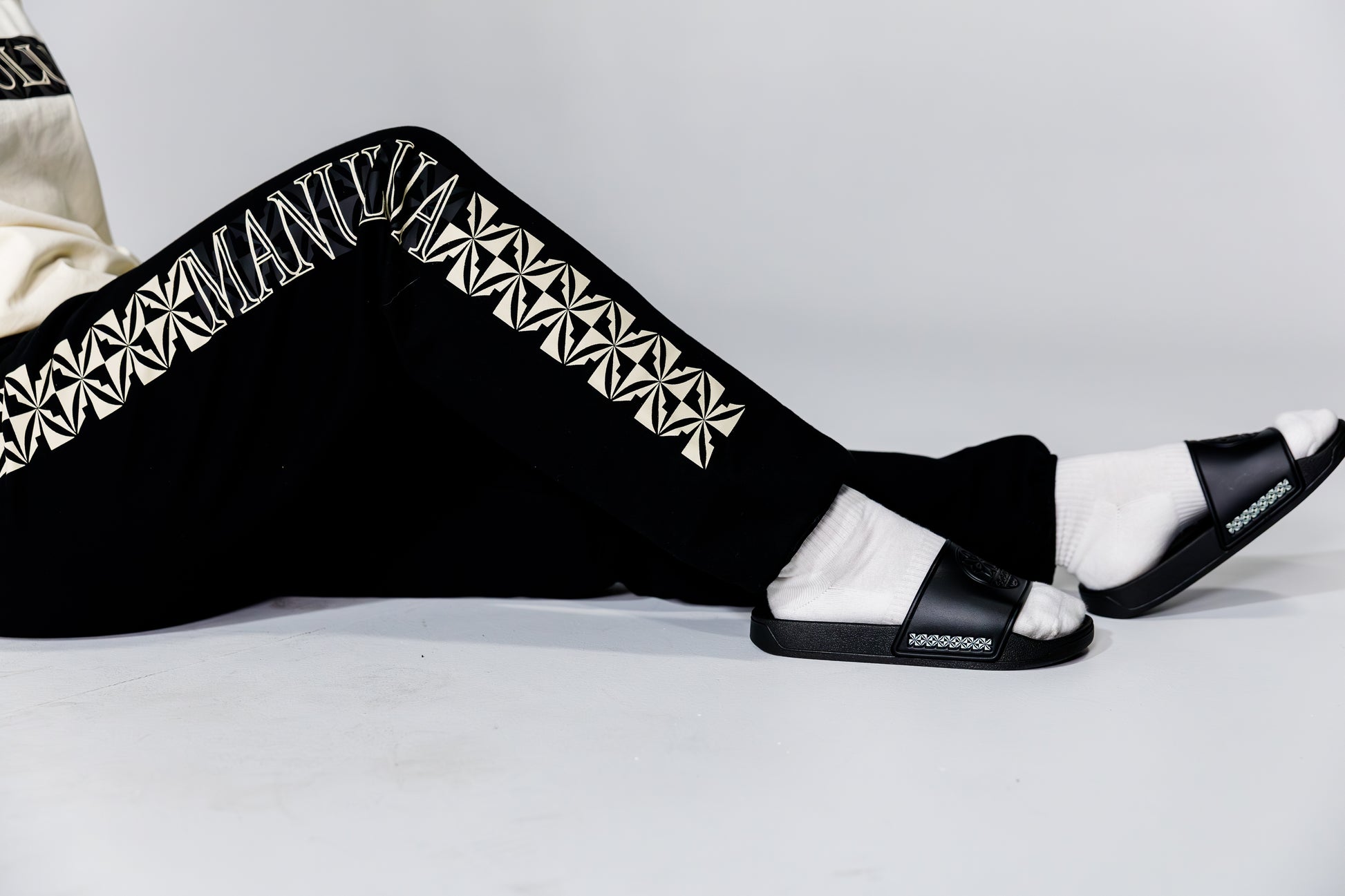 Black pants with white geometric patterns and black slides on a light gray background