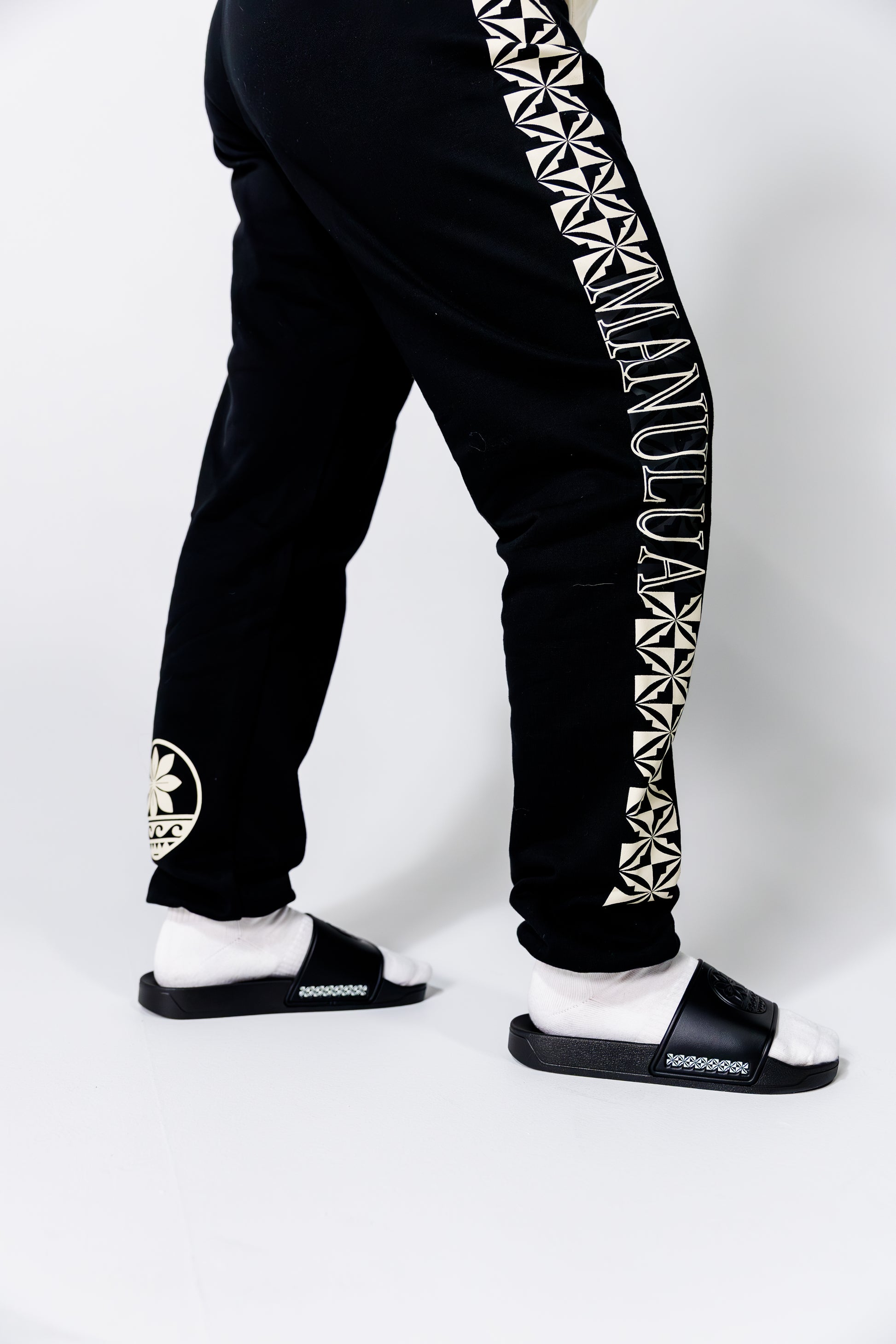 Black jogger pants with white geometric patterns and text on a white background