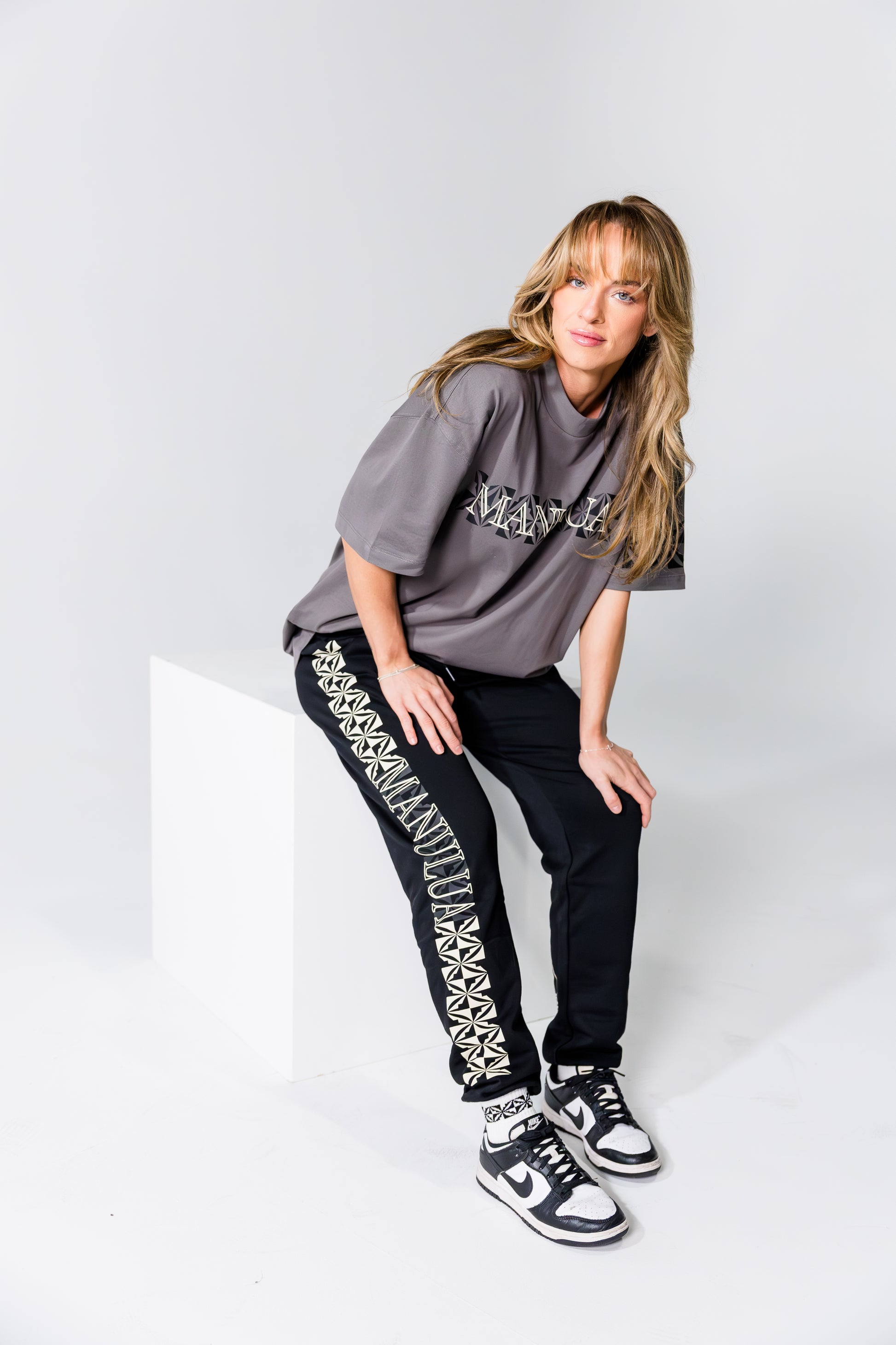 Woman wearing a gray oversized t-shirt and black pants with white patterns on a white background